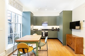 A compact kitchen with a dining area, featuring a wooden table, chairs, and a built-in oven. - Stylish Flat near Denmark Hill (London)