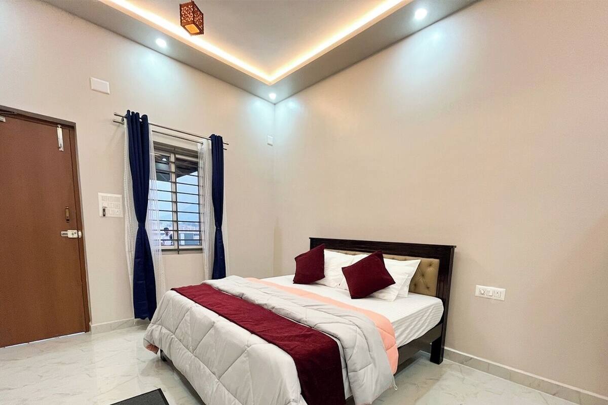 A bedroom with a bed, a desk, a window with curtains, and a door.