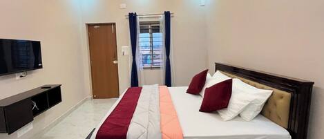 Un dormitorio con cama, televisor, armario y ventana con cortinas.