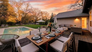 Un comedor con piscina, mobiliario exterior y vistas al atardecer.