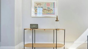 Ett konsolbord i trä med en radio och en lampa med glasskärm, placerat framför en vägg där ett inramat fotografi hänger.