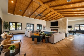 A spacious living area with a fireplace, wooden ceiling beams, and large windows. - Desert Retreat | Resort Pool + Spa + Firepit + Coworking Lounge | Near Coachella (La Quinta)