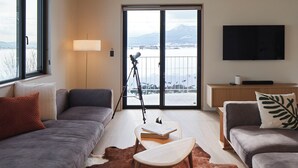 A modern living room with a large window, a sofa, a coffee table, and a TV. - Villa Matsu by H2 Life (Nakafurano)