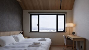 A hotel room with a large window, a bed, a desk, and a chair. - Villa Matsu by H2 Life (Nakafurano)