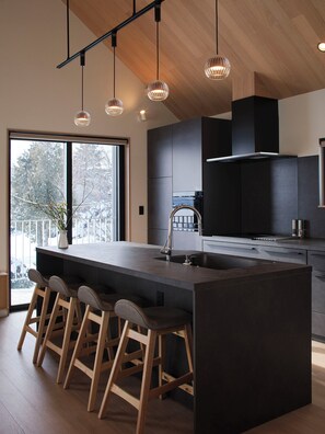 A modern kitchen with a large island, bar stools, and pendant lighting. - Villa Matsu by H2 Life (Nakafurano)