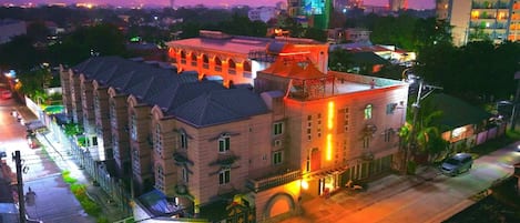 A multi-story building with a prominent central tower, a large courtyard, and a street in front.