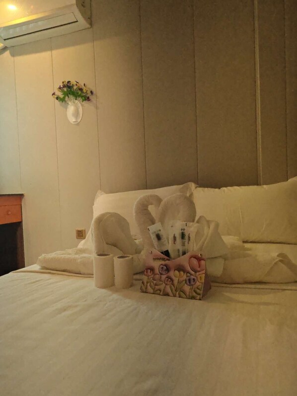 A neatly made bed with white linens, a floral-patterned pillow, and a small bedside table with a vase of flowers.