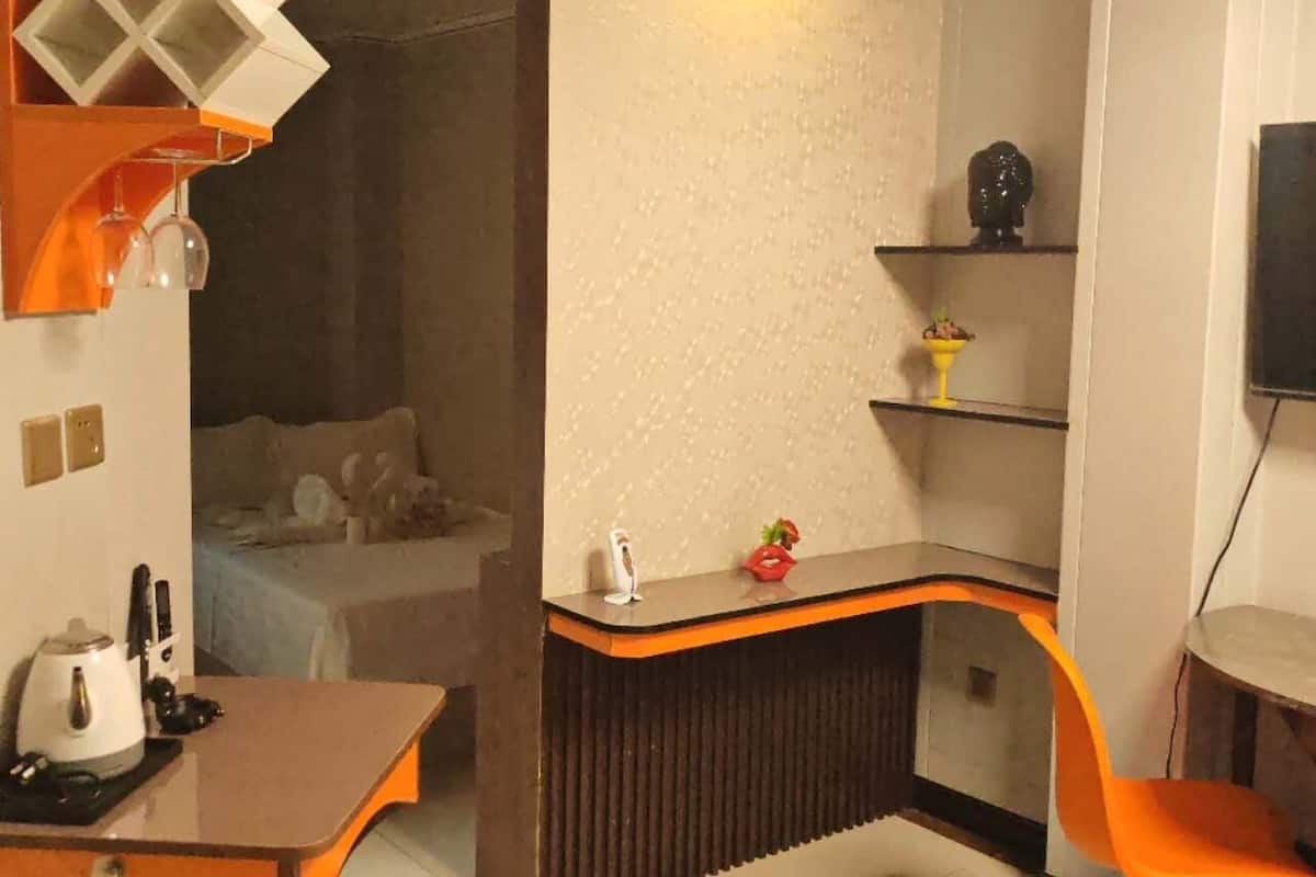 A compact hotel room with a kitchenette, a bed, a small seating area, and a TV.