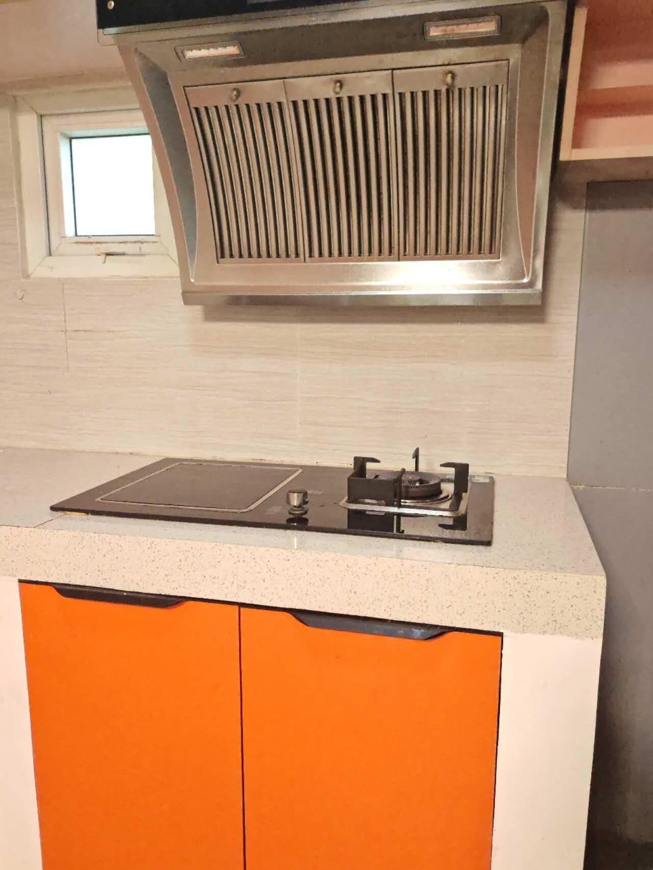 A kitchen with a built-in stove, a window above the sink, and orange cabinets.