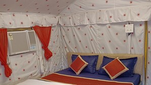 A bed with a blue and white bedspread, red and blue pillows, and a red curtain. - Down Valley Resort (Rishikesh)