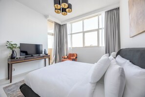 Een hotelkamer met een bed, een bureau met een televisie, een stoel en een groot raam met gordijnen.