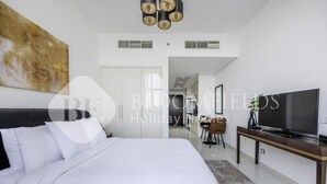 A modern hotel room with a large bed, a flat-screen TV, and a dining area visible through an open door. - Bloomfields Cozy Stu Damac (Dubai)