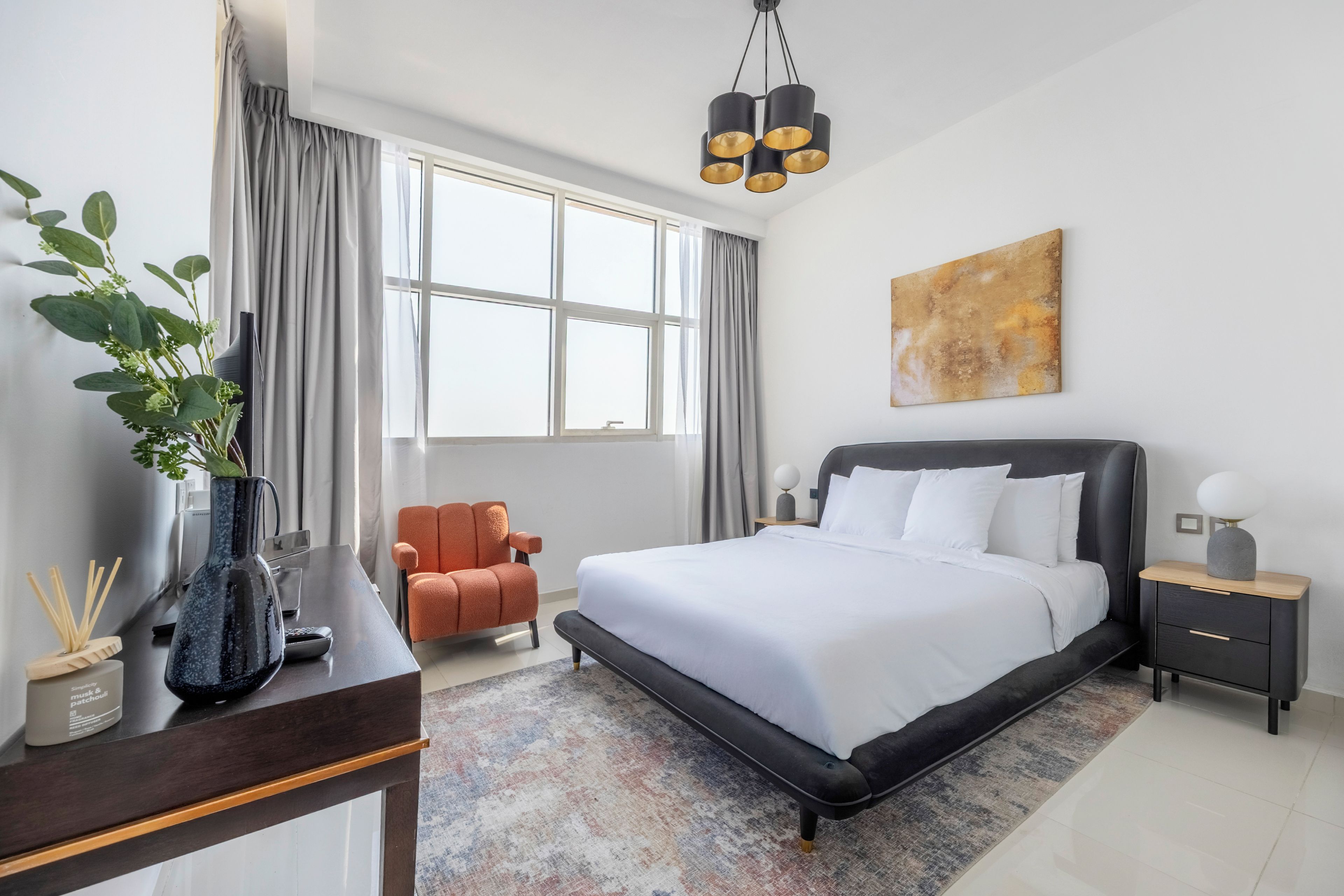 Ein modernes Hotelzimmer mit einem großen Bett, einem Schreibtisch mit einer Vase, einem Sessel und einem Gemälde an der Wand.