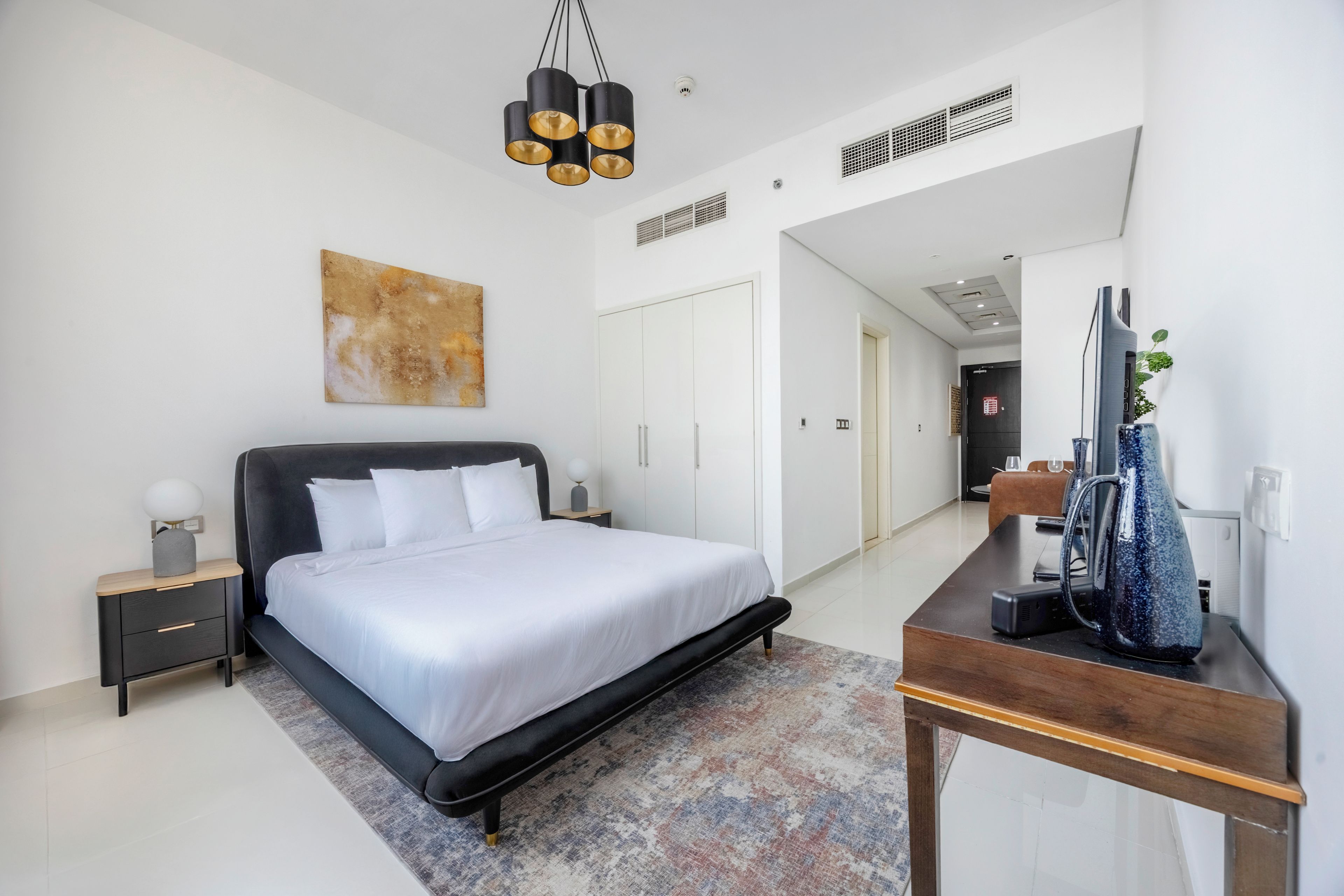 Une chambre moderne avec un grand lit, des tables de chevet, un bureau et un luminaire suspendu.