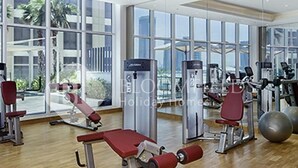 A gym with various exercise equipment, large windows, and a view of palm trees. - Bloomfields Cozy Stu Damac (Dubai)