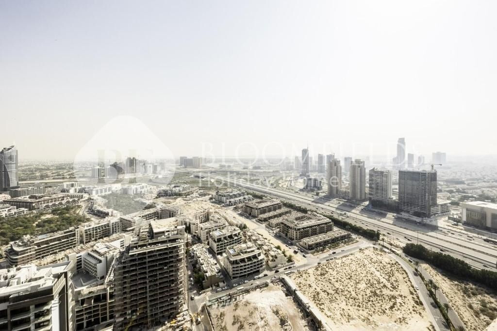 An aerial view of a cityscape with various buildings, including high-rise structures and lower buildings, roads, and undeveloped land.