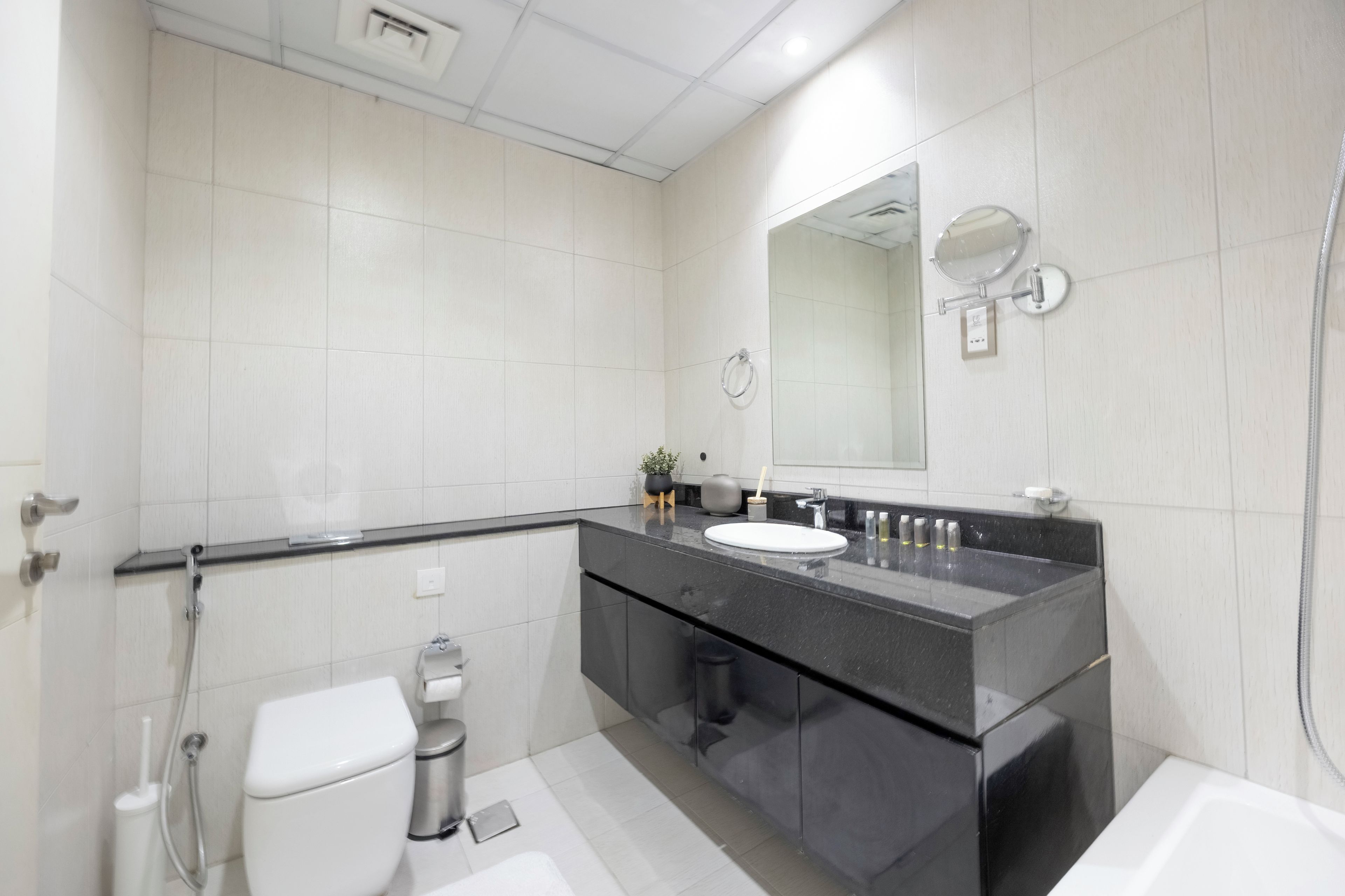 A modern bathroom with a black countertop, white tiles, a toilet, a bidet, and a shower.
