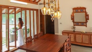 A spacious dining area with a large wooden table and chairs, a chandelier, and a decorative mirror on the wall. - Miraaya Sundara Island Villa (Kuttanad Taluk)