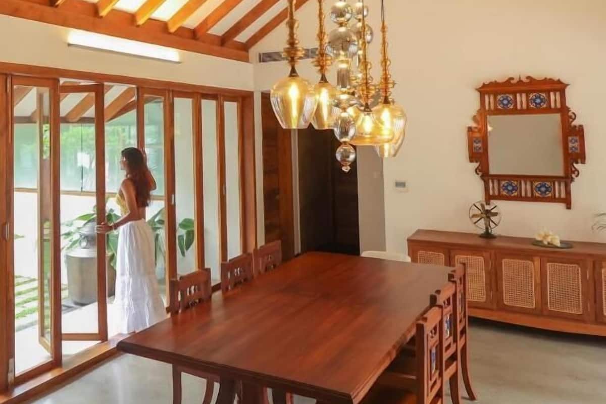 A spacious dining area with a large wooden table and chairs, a chandelier, and a decorative mirror on the wall.