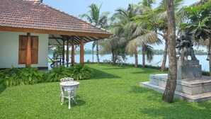 A house with a tiled roof, a lawn, a table, chairs, and a statue by the water. - Miraaya Sundara Island Villa (Kuttanad Taluk)