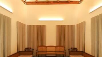 Una habitación amplia con techo alto y estructura de vigas de madera. Hay dos sofás y una mesa de centro en el centro, flanqueados por cortinas en las paredes.