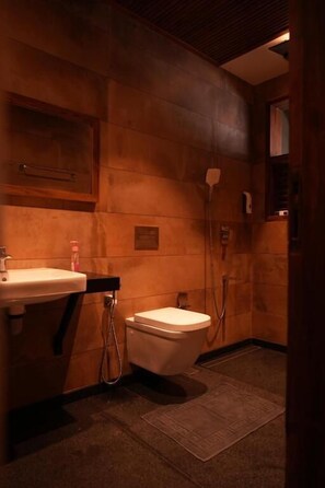 A small, dimly lit bathroom with a wooden wall, a sink, and a toilet. - Miraaya Sundara Island Villa (Kuttanad Taluk)