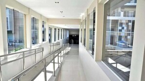 Un pasillo moderno con barandillas de vidrio, ventanas amplias y suelo de baldosas.