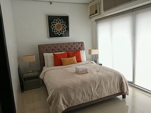 A neatly arranged bedroom with a large bed, a decorative wall piece, and a window with blinds.