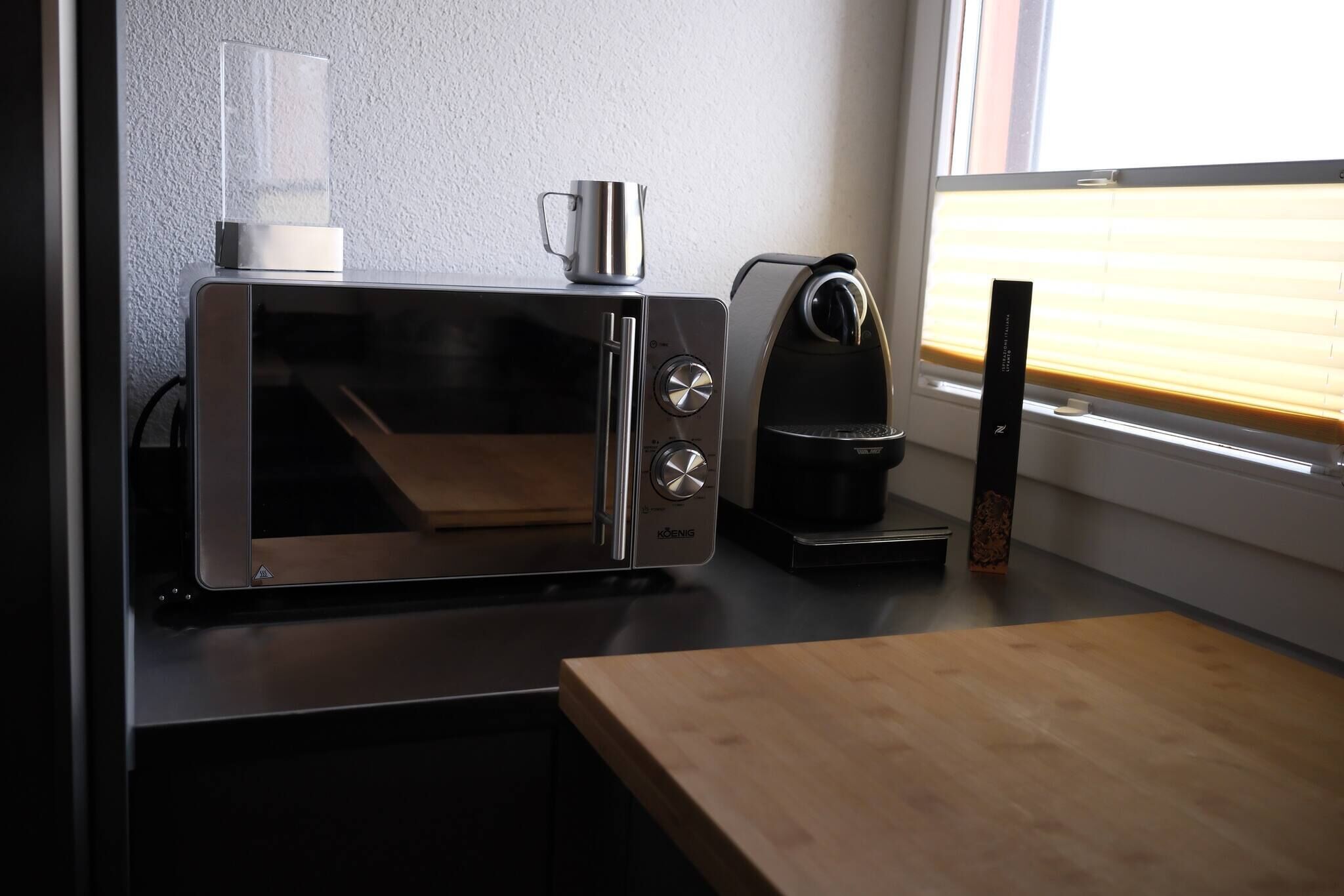 Une cuisine moderne équipée d’un four à micro-ondes en acier inoxydable, d’une machine à café et d’une bouilloire posées sur le plan de travail.