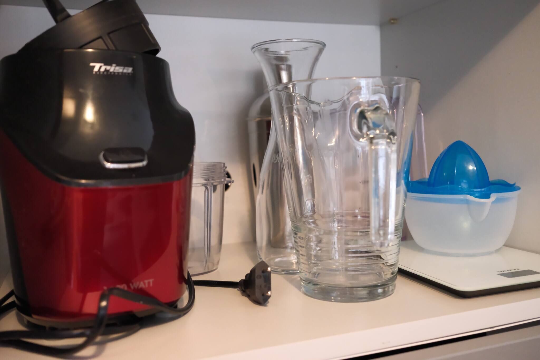 Ein roter und schwarzer Wasserkocher, ein klarer Glasbehälter und ein blau-weißer Wasserspender auf einer weißen Arbeitsplatte.