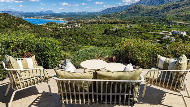 Eine Terrasse mit Tisch und Stühlen mit Blick auf eine Berglandschaft und ein weiter See.