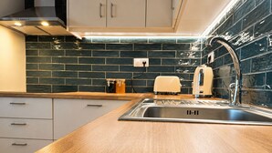 Eine moderne Küche mit Spüle aus Edelstahl, einer Holz Arbeitsplatte und einer dunklen gefliesten Spritzschutzwand.