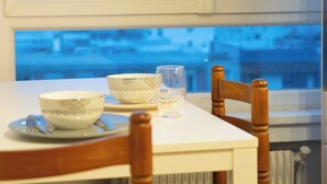 A dining table with a bowl, a glass, and a spoon, set against a cityscape view through a window. - Paris View & Direct Access  Apartment 10 people (Courbevoie)