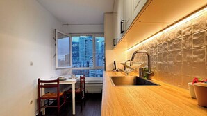 A modern kitchen with a wooden countertop, a built-in stove, and a window overlooking a cityscape. - Paris View & Direct Access  Apartment 10 people (Courbevoie)