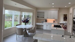 A modern kitchen with white cabinetry, a central island, and a dining area with a round table and chairs. - Dream house (Salinas)