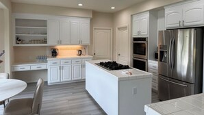 A modern kitchen with white cabinetry, a central island with a stove, and stainless steel appliances. - Dream house (Salinas)