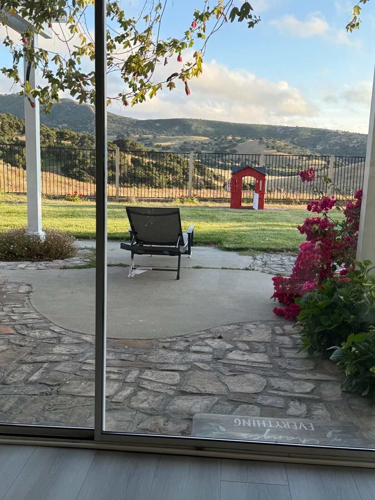 Un patio con un banco, un sendero de piedra y vistas a un área cercada con una estructura roja.