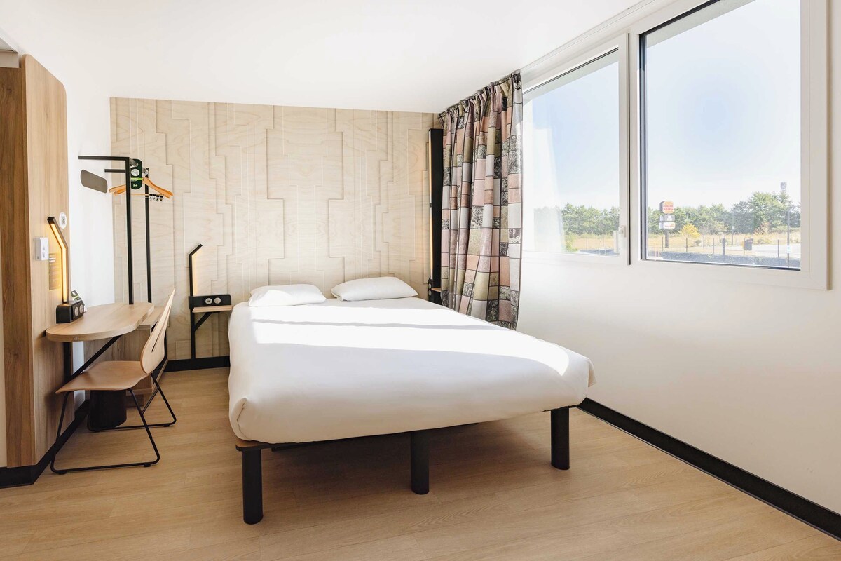 A modern hotel room with a bed, a desk, and a chair.