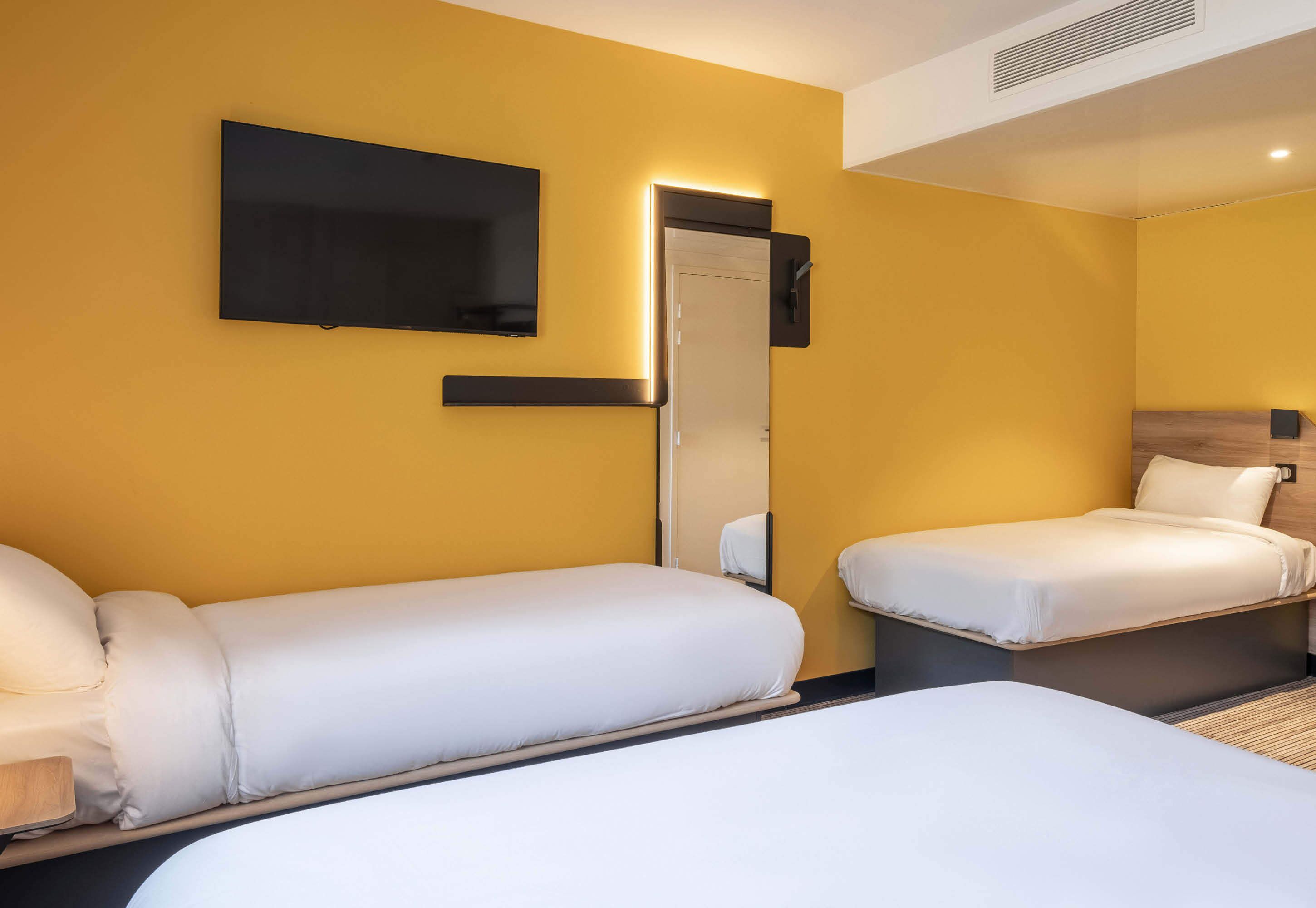 A hotel room with two single beds, a flat-screen TV mounted on the wall, and a mirror above the door.