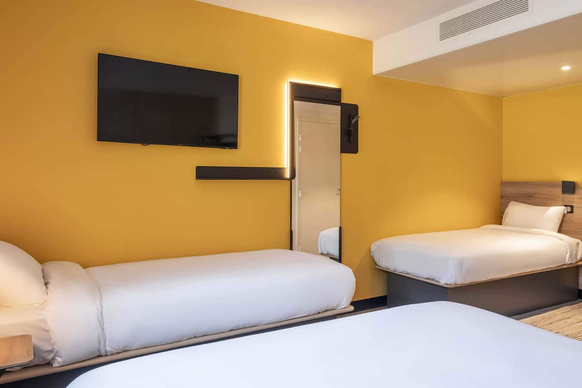 A hotel room with two single beds, a flat-screen TV mounted on the wall, and a mirror above the door.