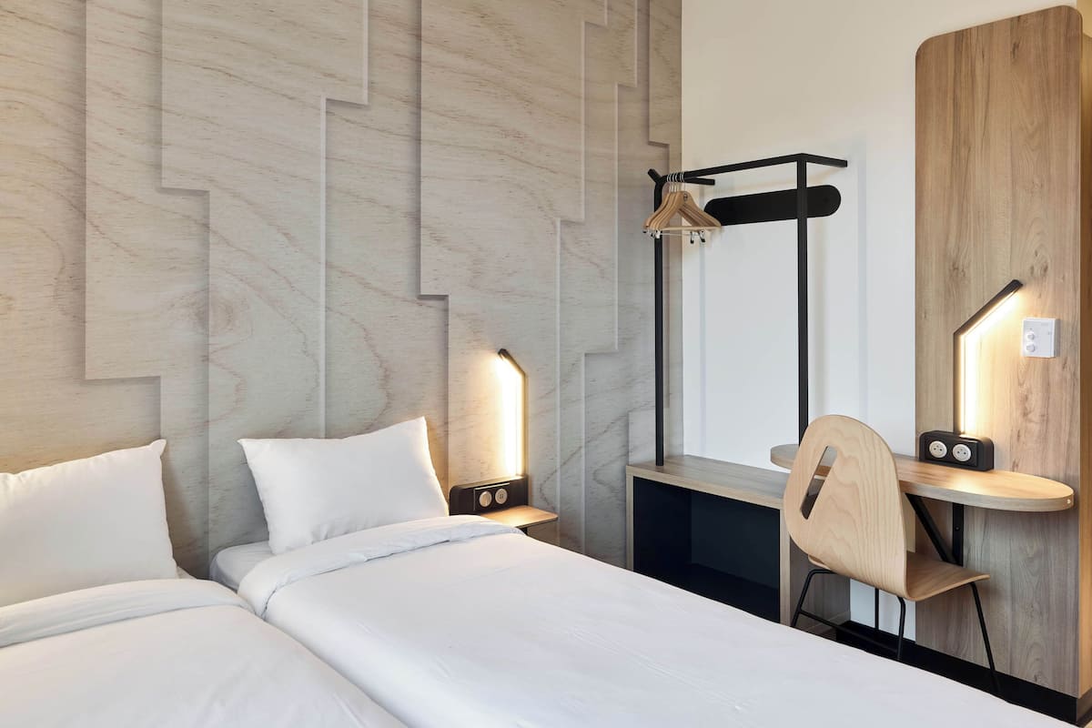 Une chambre d’hôtel avec deux lits, un bureau en bois, une chaise et un miroir.