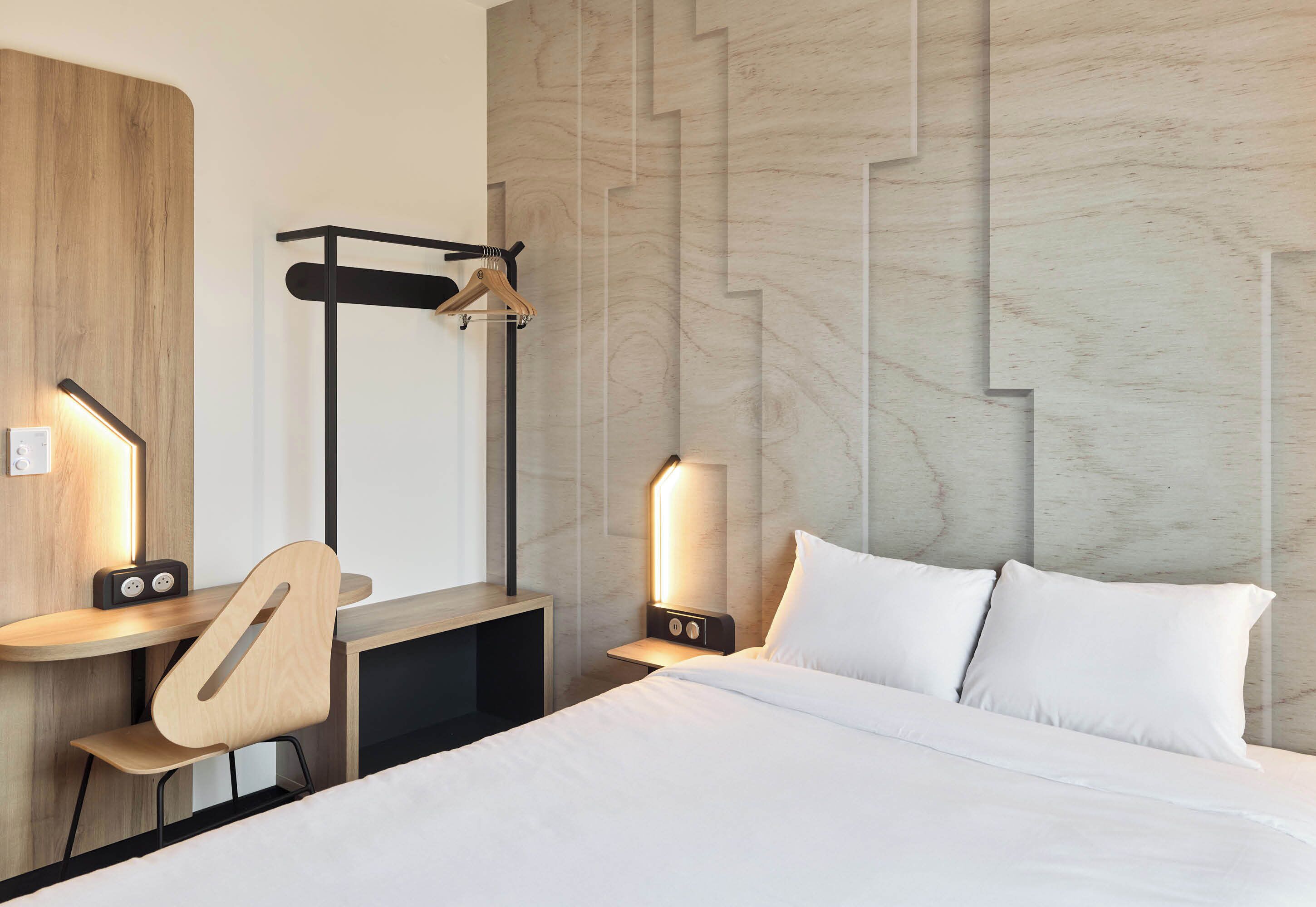 A hotel room with a bed, a desk with a chair, a guitar, and two bedside lamps.