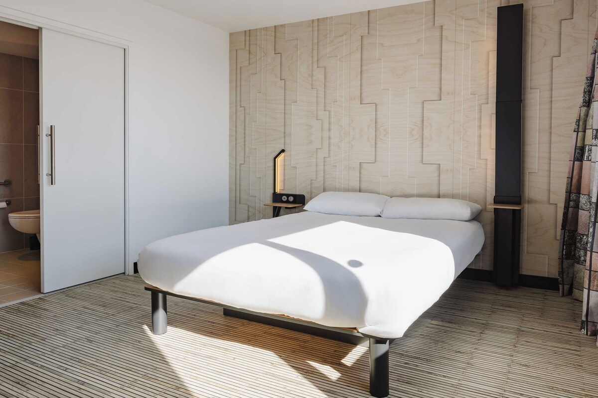 Un dormitorio moderno con cama, mesita de noche y un panel de pared de madera.