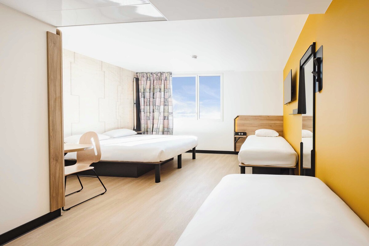 Habitación de hotel con dos camas, un escritorio, una silla y una ventana con vistas.