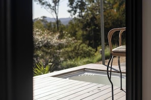 A wooden deck with a chair, a glass-top table, and a view of a garden with trees and shrubs. - SummerHill tiny home romantic escape (Bucketty)