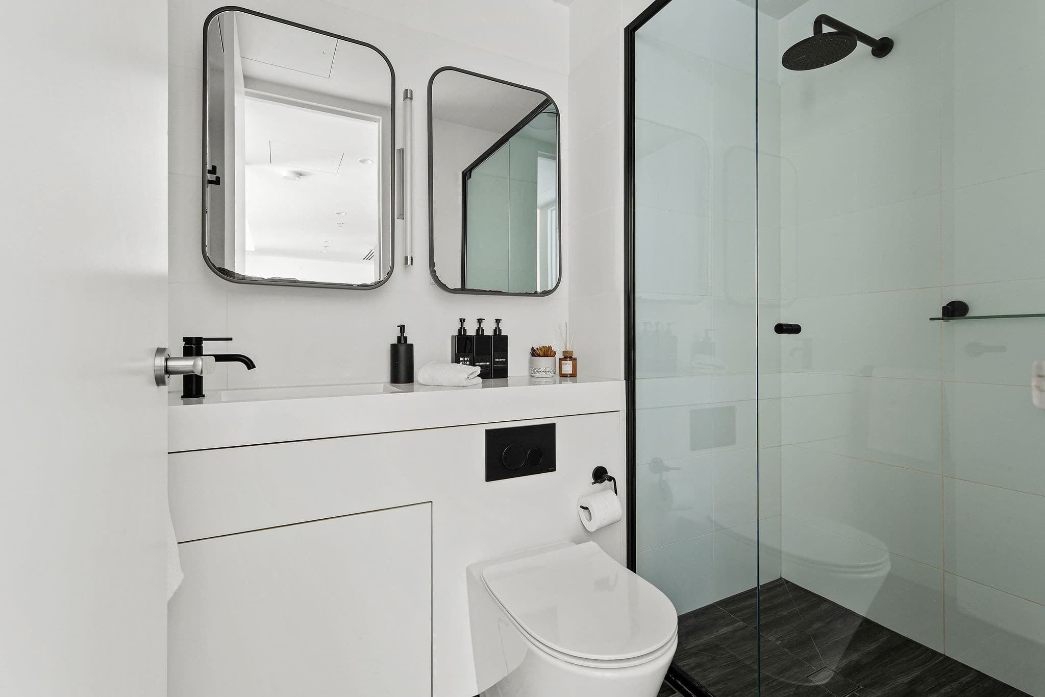 Une salle de bain moderne avec une douche à parois de verre, un lavabo blanc avec un miroir au-dessus et des toilettes.