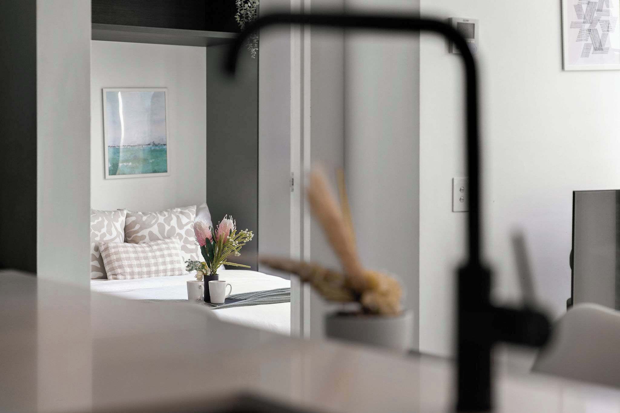 Et moderne hotelværelse med seng, et lille bord med en potteplante og et billedramme på væggen.