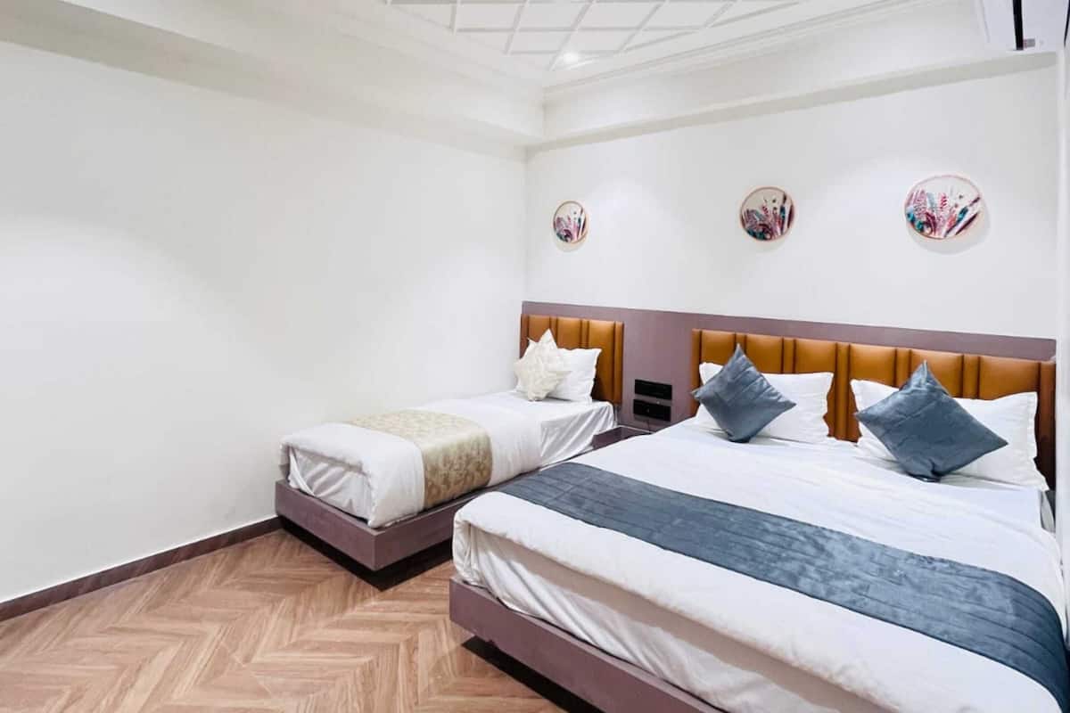 A hotel room with two beds, a wooden herringbone floor, a white ceiling with a grid pattern, and a ceiling fan.