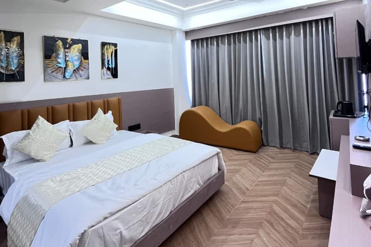 A modern hotel room with a large bed, a curved sofa, a desk with a lamp, and artwork on the walls.