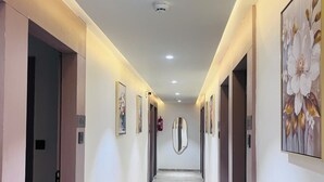 A long, narrow hallway with a marble floor, flanked by doors and walls adorned with framed artwork. - Hotel Lee Prime (Ahmedabad)
